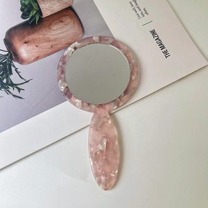 Macro shot of pink marble pattern acetate hand mirror on a minimalist white desk