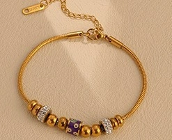 Detail of gold-plated stainless steel snake chain bracelet with purple enamel and crystals
