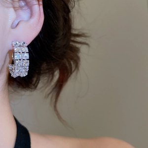 Close-up of C-shaped silver earrings with multi-row zircon crystals on a female model
