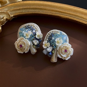 Close-up of handmade floral earrings with blue and white beads and pearls on leather background