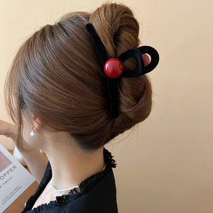 Detail view of black flocked hair claw clip with a large red bead on model's hair