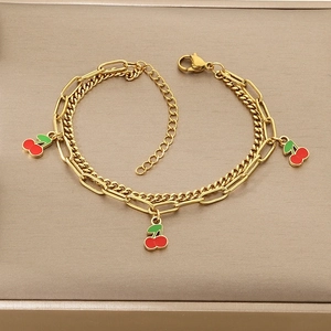 Detail of gold double-layer chain bracelet featuring red and green cherry pendants