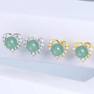 Detailed view of heart-shaped silver and gold stud earrings with green center stones