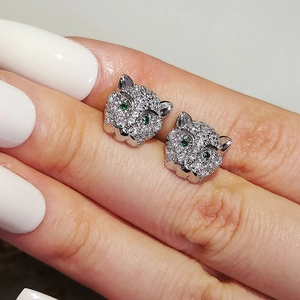 Macro shot of silver leopard head stud earrings with white zircons and green gem eyes