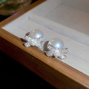 Macro shot of pearl bow earrings with silver setting in a walnut jewelry box