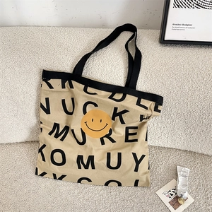 Close-up of canvas tote bag with black letters and yellow smiley face on white sofa