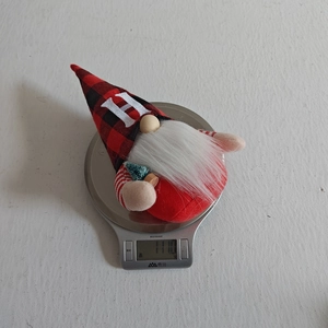 Dettaglio peluche gnomo di Natale, cappello scozzese rosso nero lettera H, decoro festivo.