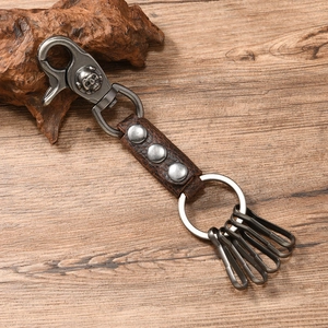 Close-up of retro leather keychain with silver skull hook and rings on wood background