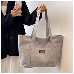 Detail of grey canvas tote bag with fashion label held by model against white wall