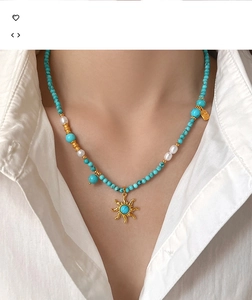 Détail d'un collier de perles turquoise et perles blanches avec pendentif soleil doré