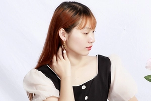 Detail of gold hollow ring earrings with white pearl pendants worn by a model