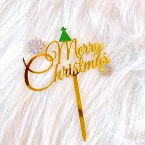 Detailed close-up of gold acrylic Merry Christmas cake topper with green glitter hat and snowflake