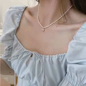 Detail of freshwater pearl necklace featuring a silver smiley face pendant on a model