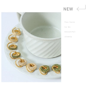 Close-up of gold geometric earrings with green and white crystals on ceramic dish