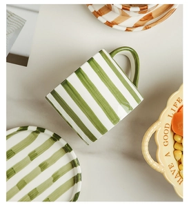 Top-down view of hand-painted green striped ceramic mug and matching saucer on marble table