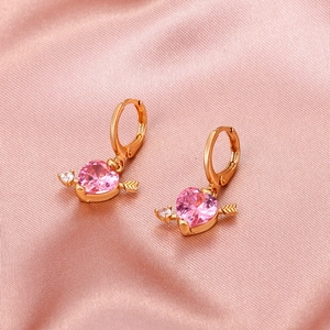 Detailed view of cupid heart earrings with pink gemstone and gold arrow on silk