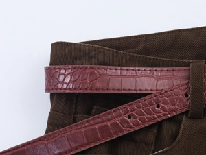 Dettaglio della cintura bordeaux testurizzata a coccodrillo su pantaloni di velluto