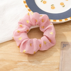 Pink fabric hair scrunchie with gold heart patterns on a rustic wooden background