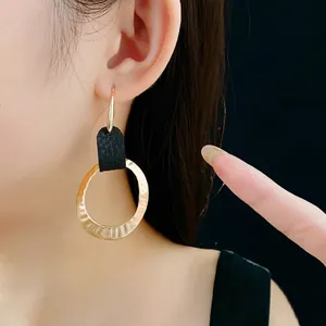 Hammered gold round earrings with black leather texture on model in dark background