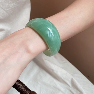 Close-up of a wide translucent light green resin bangle with cloudy marble textures