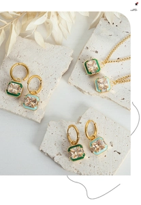Detail of gold jewelry set with emerald enamel squares and clear zircon stones