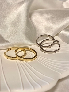 Detailed view of silver and gold round hoop earrings on white shell plate and silk