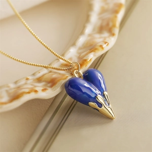 Elegant gold chain necklace with a blue heart pendant on a ceramic dish background