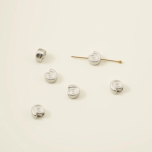 Detailweergave van zilveren spiraalvormige metalen kralen met naald voor DIY-sieraden