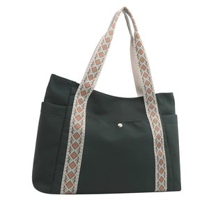 Dettaglio della borsa tote verde scuro con tracolle geometriche e tasca frontale a scatto