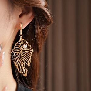 Close-up of golden hollow leaf earring with a pearl and butterfly on a model