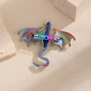 Detail of colorful iridescent dragon brooch with safety pin back on textured background