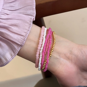 Close-up of bohemian layered beaded bracelets in pink, white, and gold on a wrist