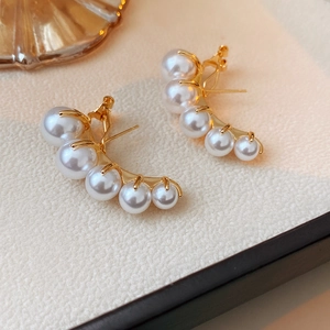 Detail shot of curved gold earrings with five graduated white pearls on a light surface