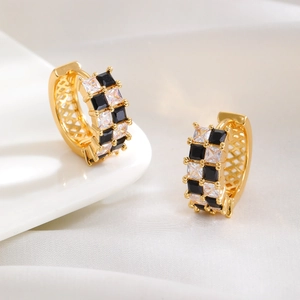 Macro shot of gold checkered earrings with black and white zircon on white silk