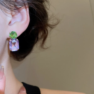 Detail of elegant two-tone earrings featuring green round and purple square gemstones