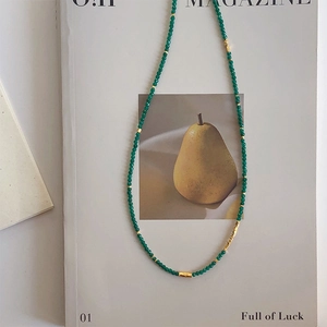 Vintage green beaded necklace with gold accents on a minimalist artistic background