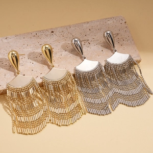 Polished gold and silver fan-shaped fringe tassel earrings on a textured stone tray