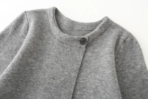 Dettaglio del cardigan in maglia grigia con scollo a V, trama e bottone nero in primo piano