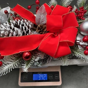 Detailed view of Christmas wreath with red bow and pinecones weighing 342 grams on scale