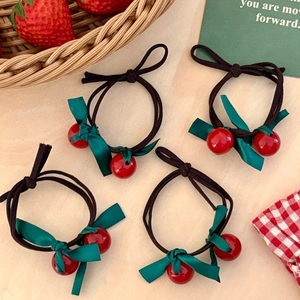 Elastic hair ties with green ribbon bows and red cherry beads on wood background