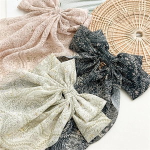 Detail of three paisley bow hair clips in pink, white, and black chiffon fabric