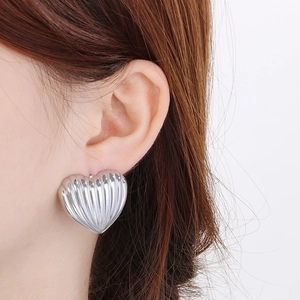 Macro shot of silver heart stud earrings with vertical ribbed texture on a model