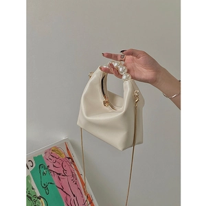 Detail of beige pillow bag with pearl handle, heart zipper, and gold chain strap