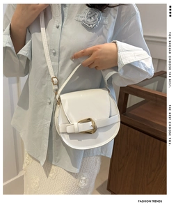Close-up of a white patent leather crossbody bag with a distinctive gold horseshoe buckle