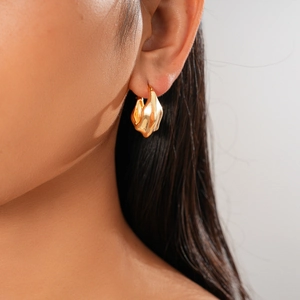 Détail de boucles d'oreilles créoles dorées en forme de cœur portées par un mannequin