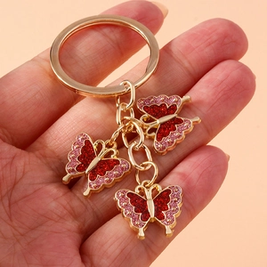 Detailed close-up of three red butterfly keychains with gold metal frames held in hand
