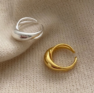 Detailed view of intertwined wide-band silver and gold rings on a beige knit texture