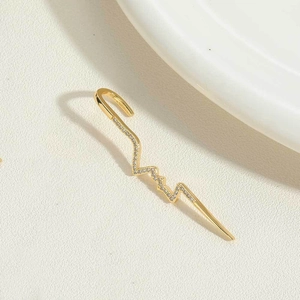 Detail eines goldenen Ear Cuffs mit elegantem Herzschlagmuster und funkelnden weißen Zirkonia