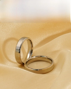 Close-up of stainless steel couple rings with brushed finish on champagne silk fabric