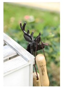 Detail of vintage cast iron deer head hook holding a gardening tool against a wood box